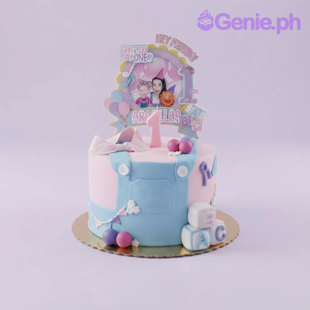 First Birthday Bow Cake Pink and blue 1-tier fondant cake with a personalized photo printout topper, a number 1 candle, and edible block decorations.