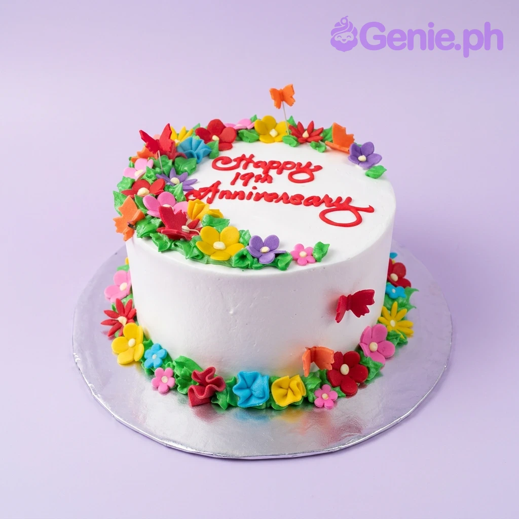 Anniversary White Floral Cake A white round 1-tier cake themed around Anniversary, featuring colorful gumpaste flowers, butterflies, red icing text, and green leaves.