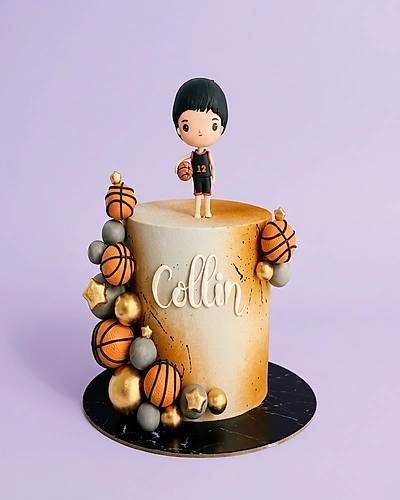 Tall basketball themed cake with a 3D boy figurine, basketball spheres, and gold stars on a gradient orange and white icing base.