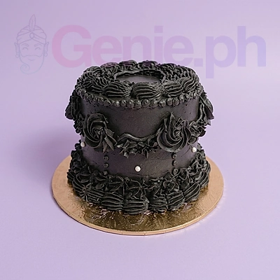 Elegant all-black vintage style cake with intricate piped icing ruffles, rosettes, and small white pearl accents on a gold base.