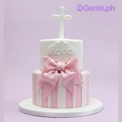 Christening Bow 2-Tier Cake A two-tier white and pink fondant christening cake with a large pink bow, a white cross topper, and a name plaque.