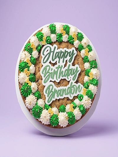 Round chocolate chip cookie cake with green and white icing rosettes and a Happy Birthday Brandon topper.
