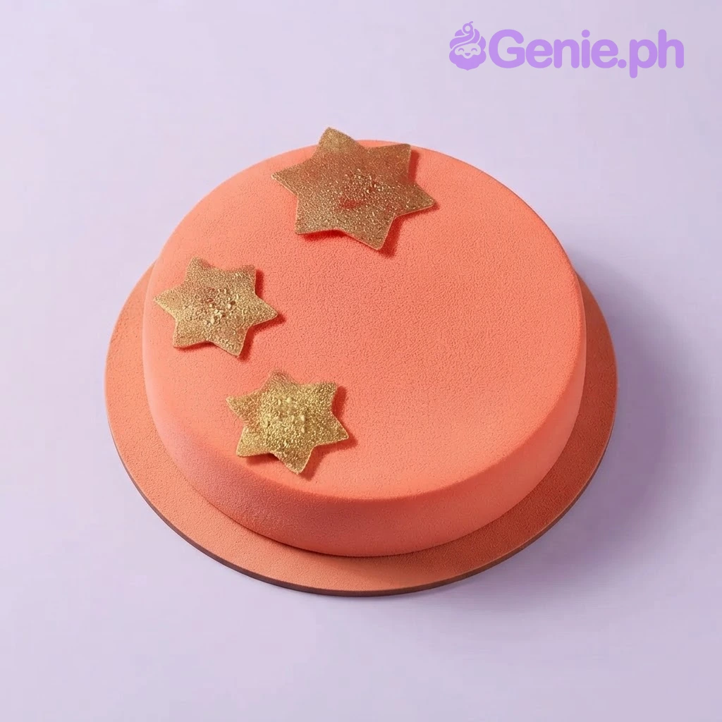 Coral Star Glitter Birthday Cake Coral round cake with three gold glitter star toppers on a wooden board