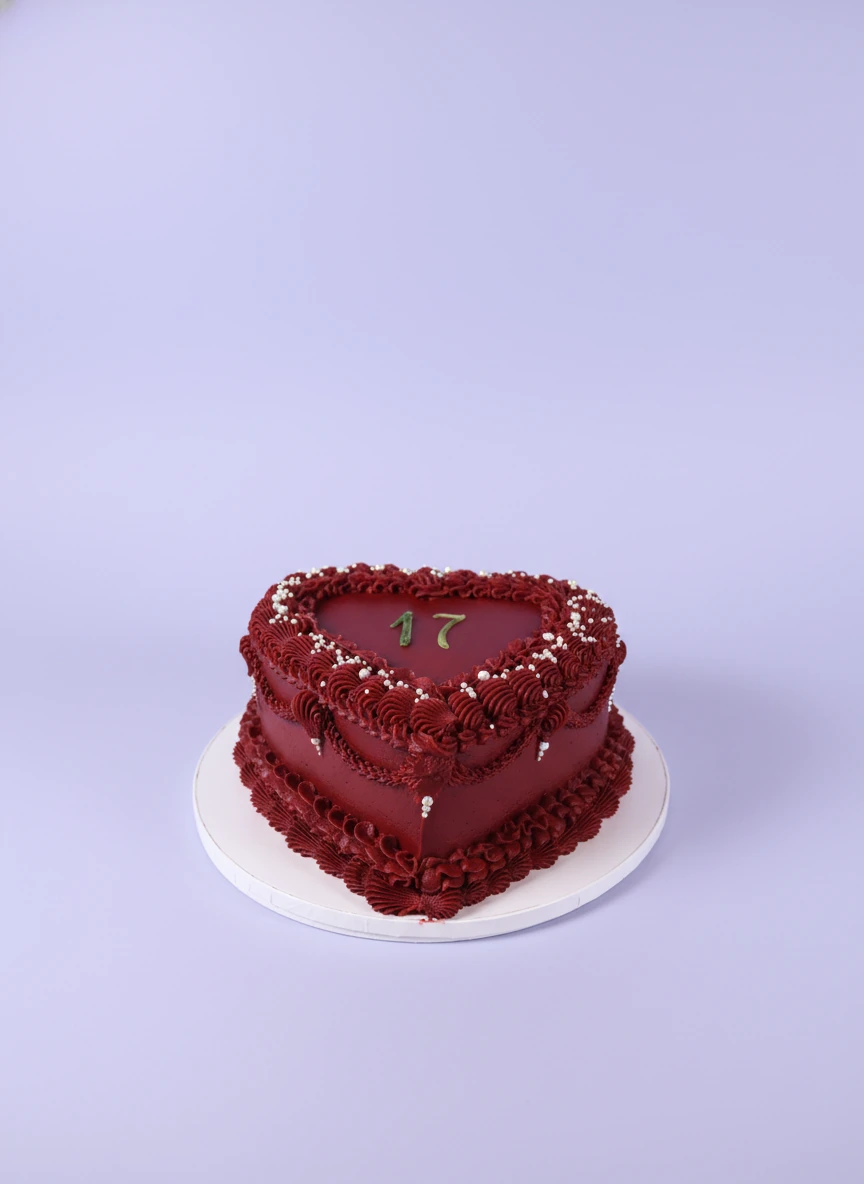 Dark Red Heart Maroon Birthday Cake A dark red heart-shaped 1-tier cake, with a gold '17' topper, piped borders, and white pearl sprinkles.