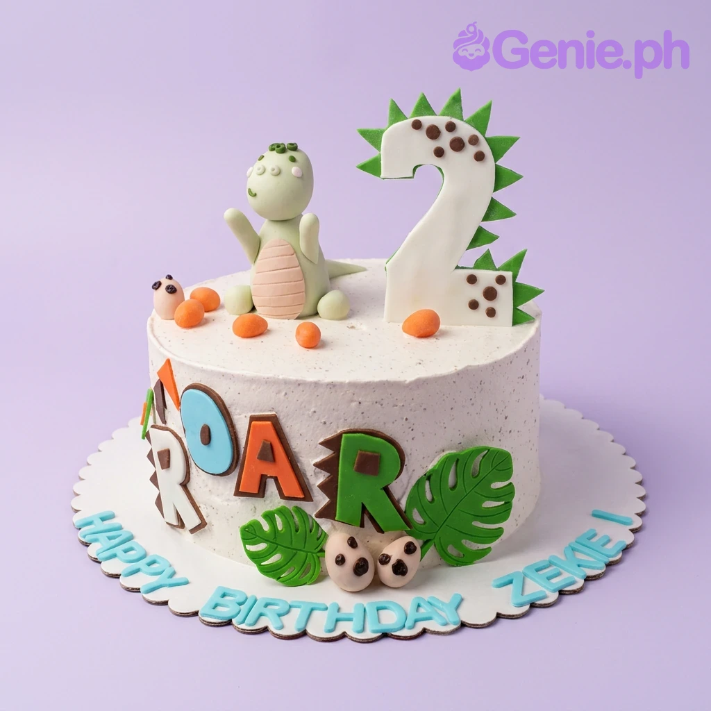 Dinosaur White Birthday Cake A white 1 Tier cake themed around Dinosaurs, with a green fondant dinosaur, a large number 2 topper, and colorful ROAR letters.