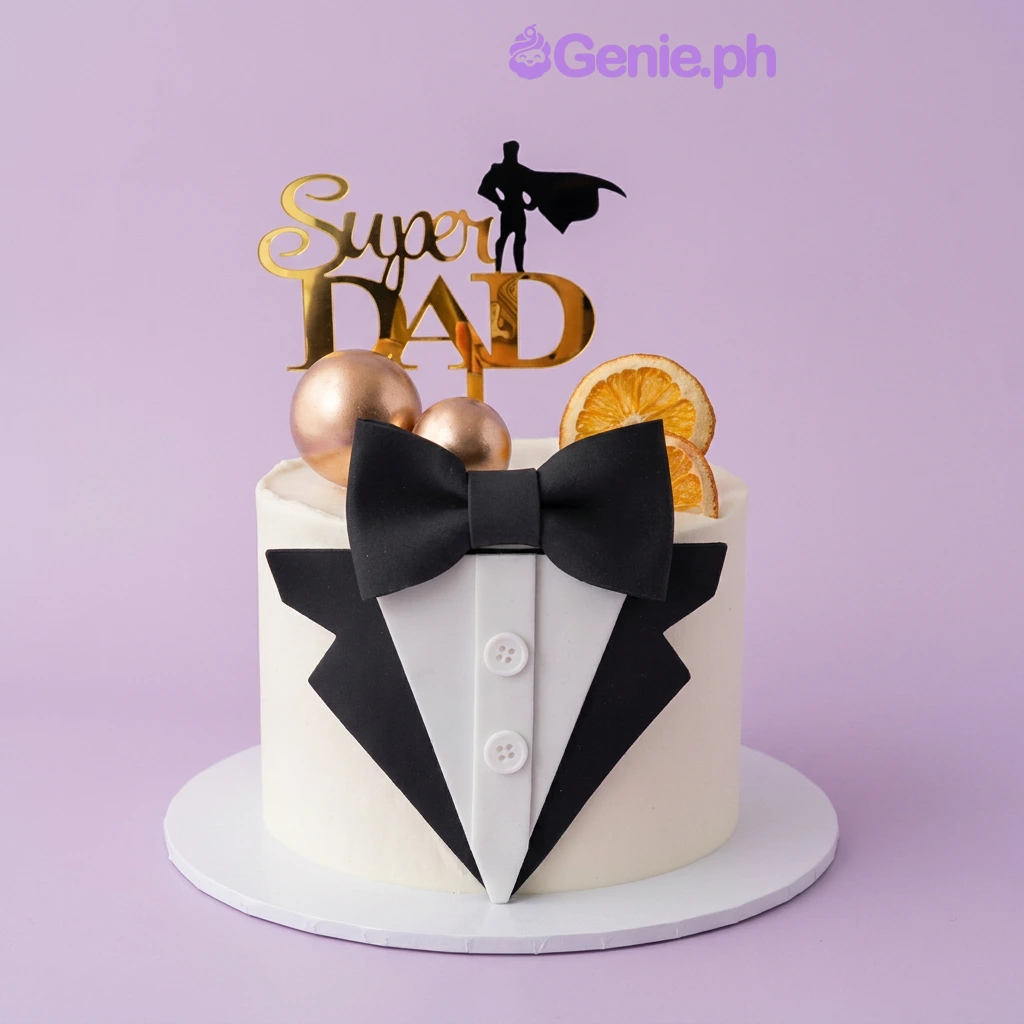 Father's Day White Bow Cake White single-tier cake with a gold Super Dad topper, black fondant bow, tuxedo shirt panel, gold spheres, and dried orange slices