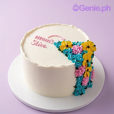 Floral Minimalist White Birthday Cake White single-tier cake with pink Mom's Slice message and colorful piped floral cascade on the side