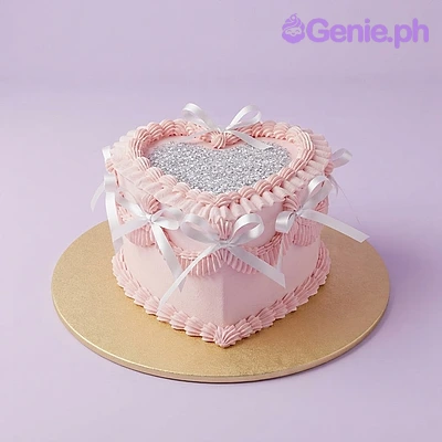 Heart Light Pink Birthday Cake Light pink heart-shaped cake with soft icing, ruffled borders, white satin ribbon bows, and a silver glitter top.
