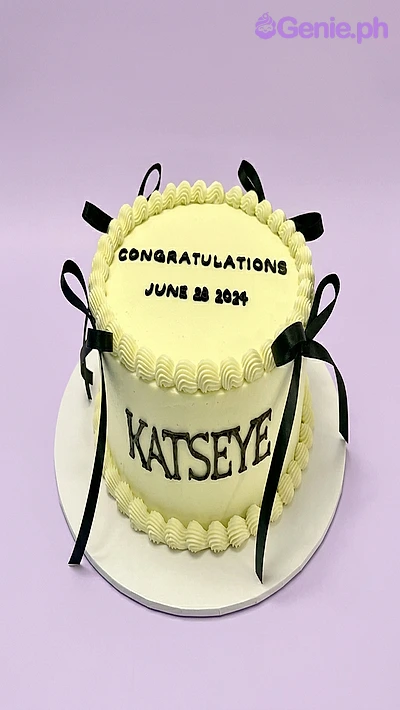 Katseye-Inspired Congratulations Birthday Cake Light yellow single-tier cake with black piped text and black satin ribbon bows