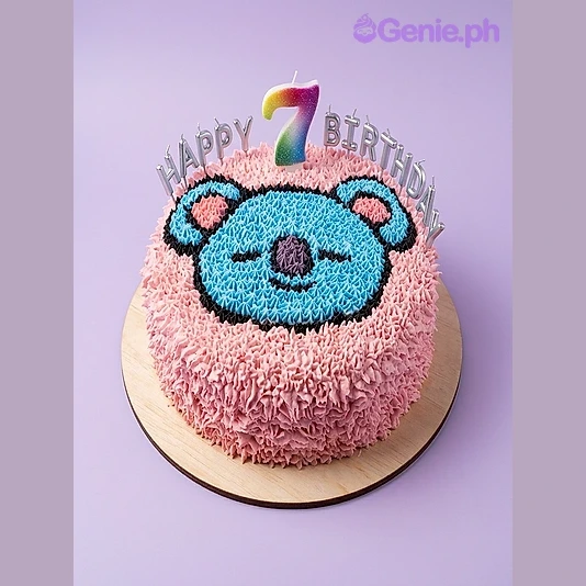 Koala Cake Koala cake with a piped blue koala face, rainbow number 7 candle, silver happy birthday banner, and pink rosettes