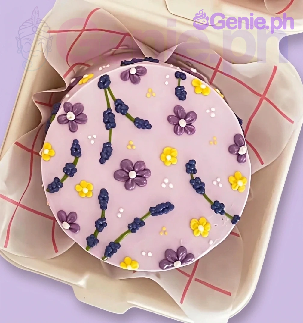 Lavender Floral Bento Cake A light purple bento cake with a lavender floral theme, featuring piped purple and yellow flowers, green stems, dark blue buds, and white icing dots.