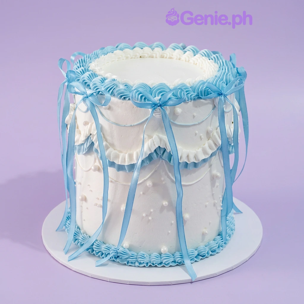 Minimalist Blue Pearl Cake White 1-tier cake with soft icing, light blue satin ribbon bows, piped blue icing swags, and white pearl accents