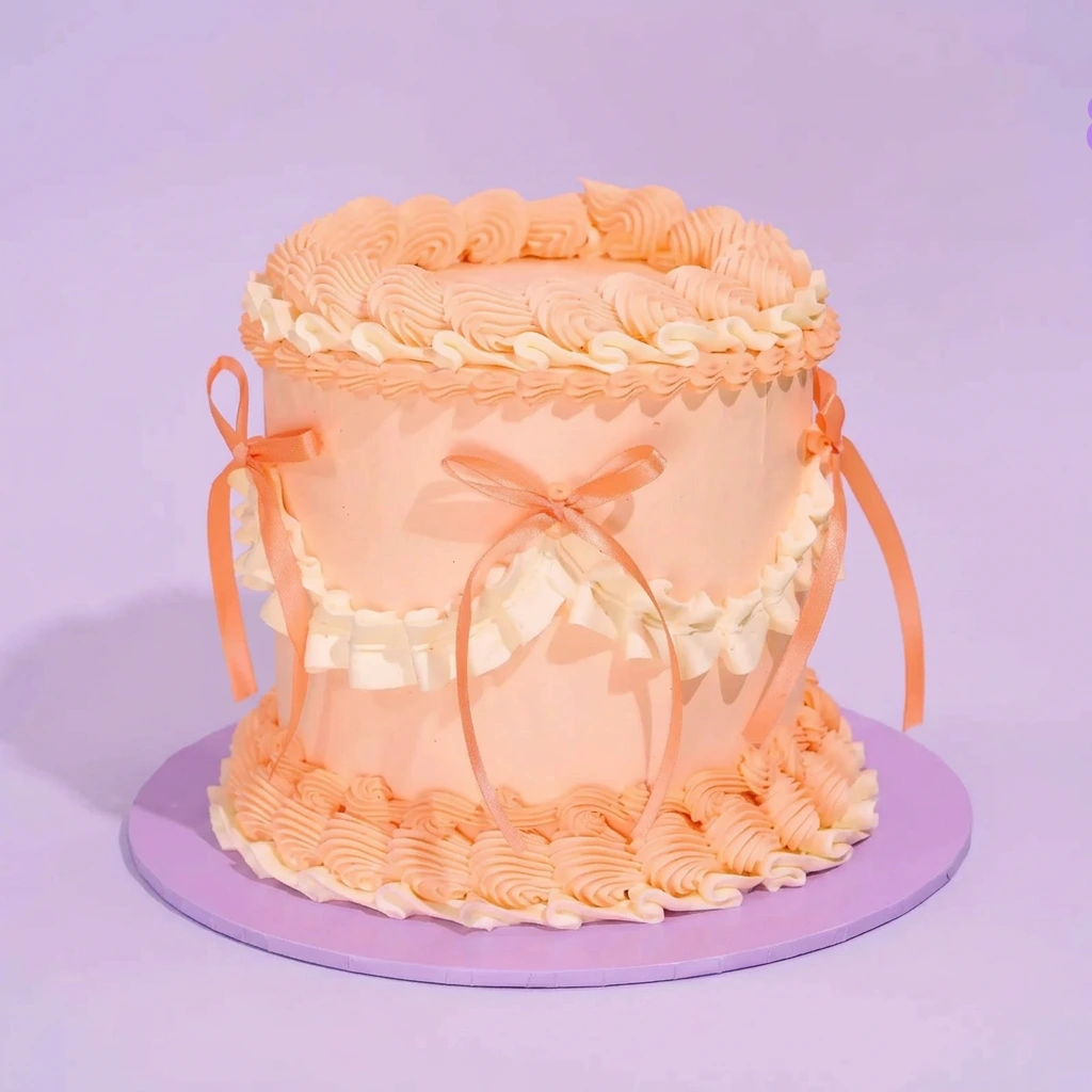 Peach Ruffle Cake Peach 1-tier cake with piped icing ruffles and satin ribbon bows on a pink cake board