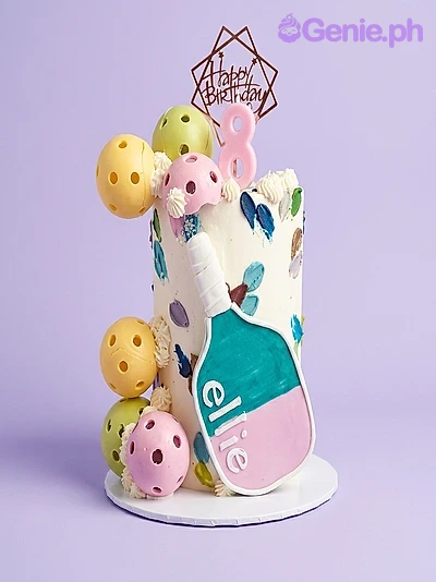 Pickleball Birthday Floral Cake White single tier cake with a pickleball paddle topper, pink number 8 candle, and colorful pickleball spheres