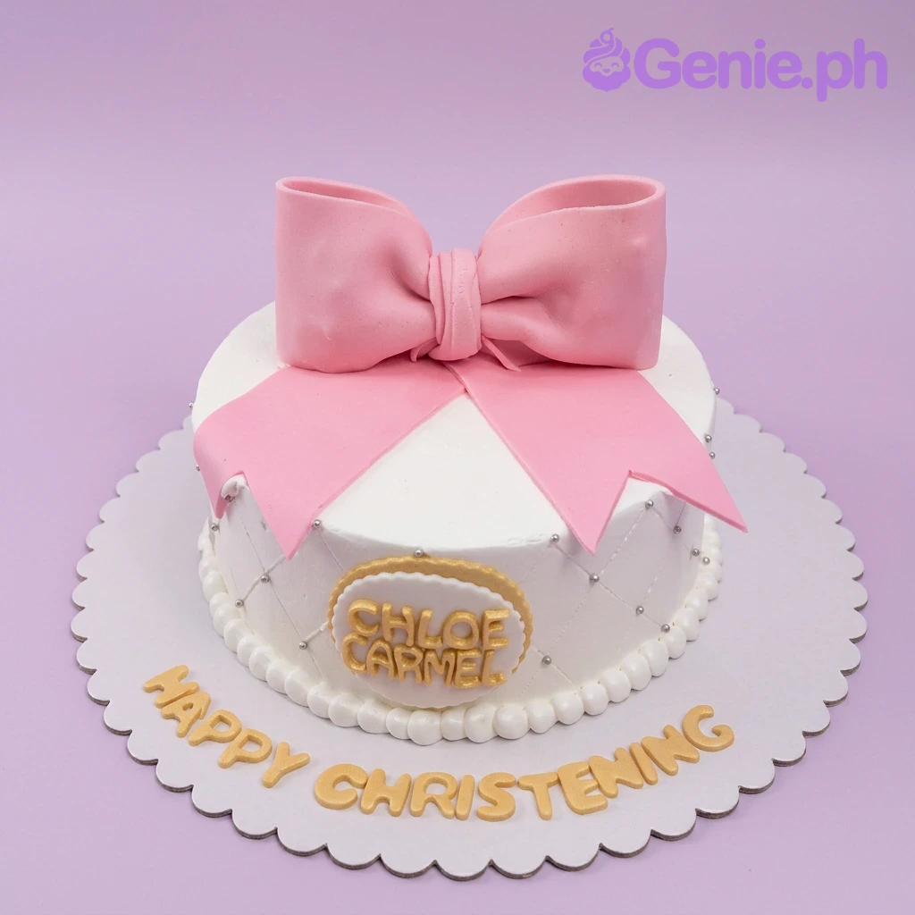 White 1-tier christening cake with a large pink fondant bow, silver dragees, and gold lettering on a scalloped base board.