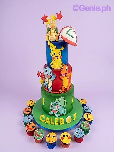 A multicolor 3 Tier cake featuring a Dragonite figure, an Ash Ketchum hat, Pikachu, Squirtle, Charmander and Bulbasaur printouts, gumpaste letters, fondant stars and lightning bolts.