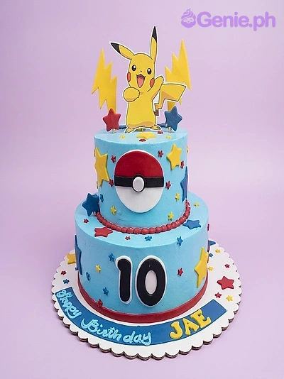 Pokemon-Inspired Pikachu Sky Blue 2-Tier Cake A light blue 2-tier cake featuring Pikachu and Pokeball printouts, yellow lightning bolts, colorful stars, and a red beaded icing border.