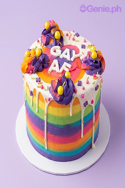 Rainbow Pride Drip Birthday Cake Rainbow striped 1-tier cake with white drip, purple icing rosettes, and white GAY AF message