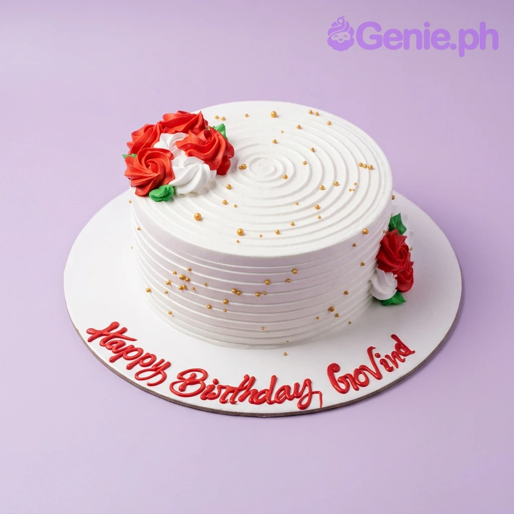 Red Rose Birthday White Floral Cake White round cake with red and white icing roses, gold dragees, and a Happy Birthday Govind message on the base board.