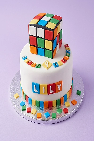 White fondant Rubik's Cube birthday cake for Lily's 9th birthday with colorful square accents and a large 3D Rubik's Cube topper. White fondant Rubik's Cube birthday cake for Lily's 9th birthday with colorful square accents and a large 3D Rubik's Cube topper.