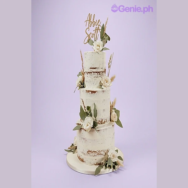 A white and green three-tier semi-naked rustic wedding cake, featuring a gold name topper, fresh white roses, and green leaves. A white and green three-tier semi-naked rustic wedding cake, featuring a gold name topper, fresh white roses, and green leaves.
