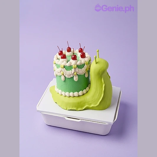 Snail Green Cake Green snail-shaped cake with cherry toppings and white piped borders on a white board