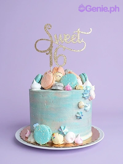 Sweet 16 Sky Blue Glitter Birthday Cake A light blue 1-tier Sweet 16 cake with a gold glitter 'Sweet 16' topper, macarons, and meringue kisses.