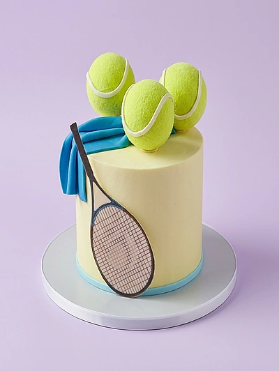 Minimalist light yellow tennis themed cake featuring three 3D fondant tennis balls, a blue fondant towel, and a tennis racket graphic.