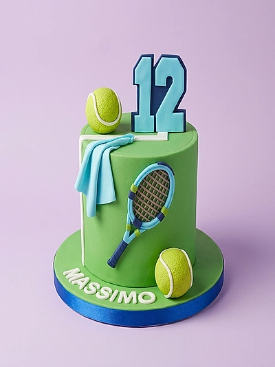 Light green tennis themed birthday cake with a blue number 12 topper, tennis balls, a racket, and a blue towel decoration.