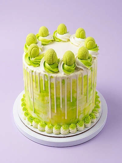 Light green and white tennis themed cake with tennis ball toppers and white icing drips.