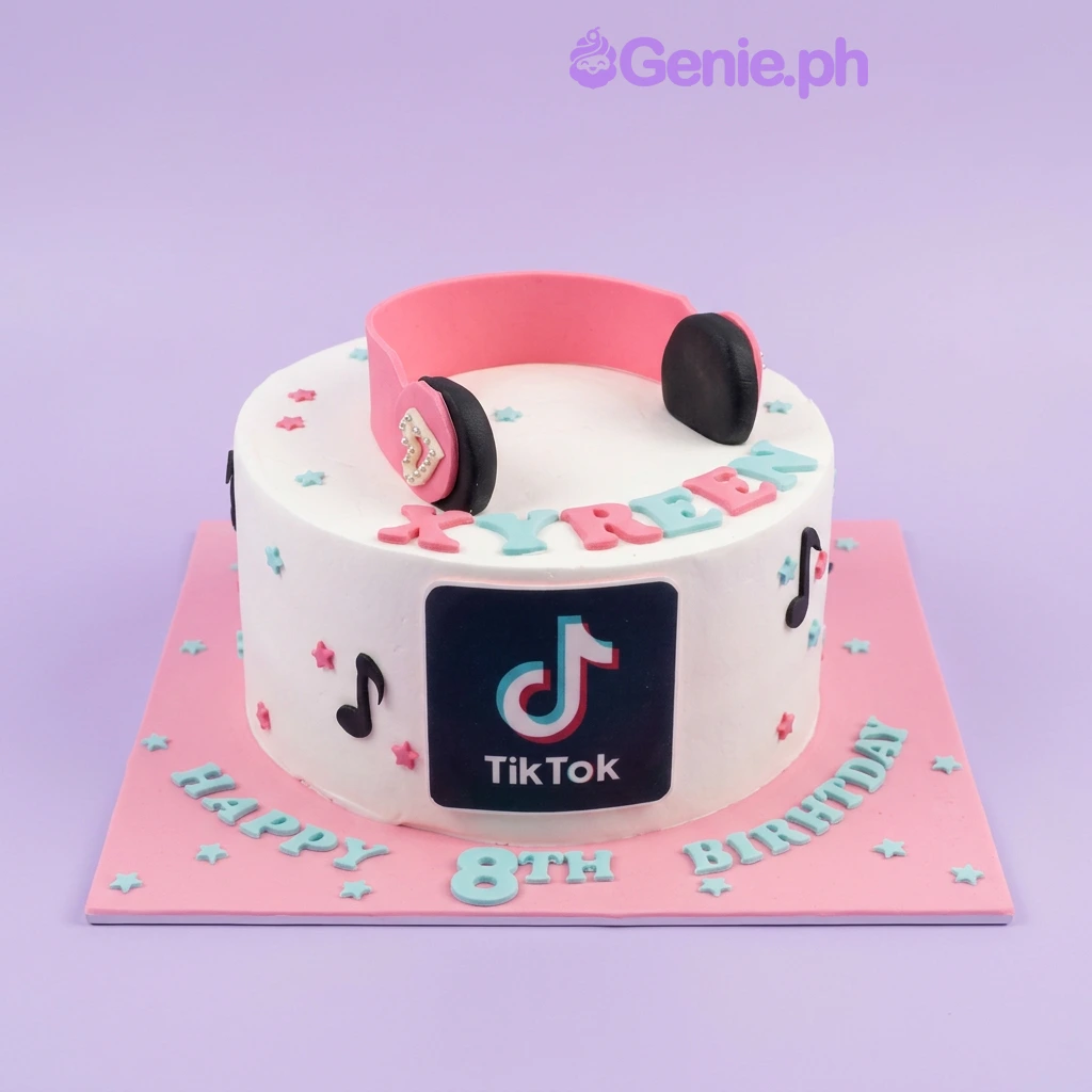 White 1-tier TikTok themed birthday cake with pink headphones, musical notes, and blue and pink lettering on a pink base board.