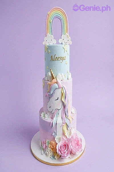 A pastel 3-tier fondant Unicorn cake with a rainbow topper, a detailed unicorn figure, pink icing roses, and gold stars.
