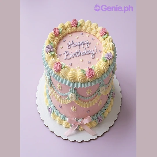 Pink one tier soft iced cake with a blue piped message, yellow rosette border, piped flowers, blue icing swags, and a pink satin ribbon bow