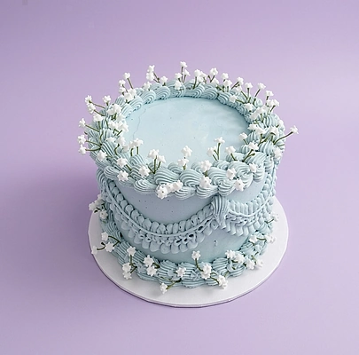 Light blue vintage style cake with intricate piped icing swags and white lily of the valley floral accents