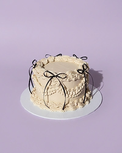 Vintage-style white minimalist cake with intricate cream piping and black ribbon bows.