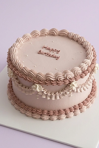 Elegant light pink vintage-style cake with intricate piped icing ruffles, swags, and a Happy Birthday message.