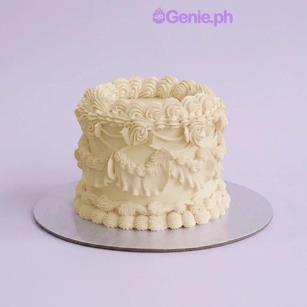 One tier ivory soft iced cake with intricate piped swags and rosettes and top and base borders