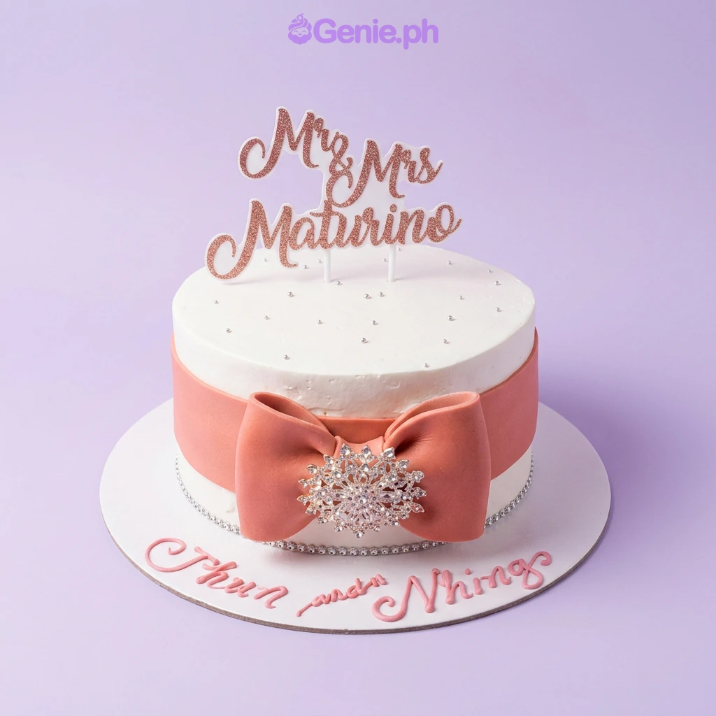 Wedding White Bow Cake A white 1-tier wedding cake, featuring a rose gold glitter Mr & Mrs Maturino topper and a peach fondant bow with a rhinestone brooch.