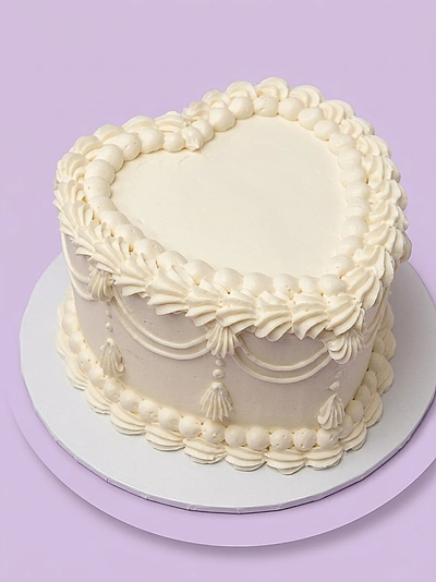 White heart-shaped vintage cake with intricate piped icing swags and borders