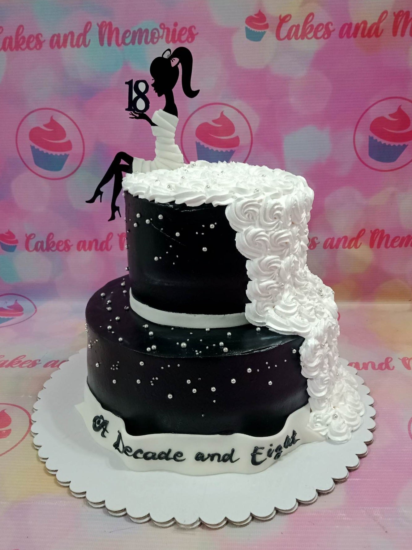 Elegant black and white 2-tier 18th birthday cake with a silhouette topper and cascading white icing rosettes. Elegant black and white 2-tier 18th birthday cake with a silhouette topper and cascading white icing rosettes.
