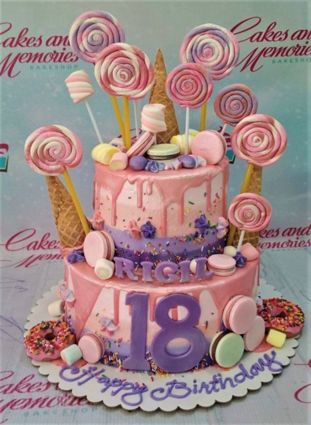 Two-tier pink and purple ombre cake decorated with lollipops, macarons, donuts, and a large purple number 18. Two-tier pink and purple ombre cake decorated with lollipops, macarons, donuts, and a large purple number 18.
