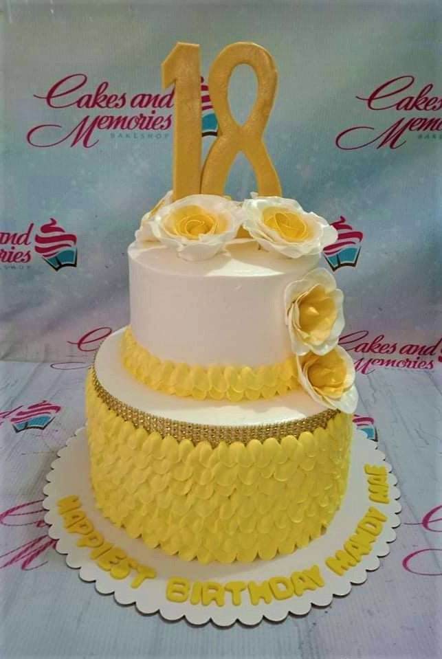 Yellow and white 2-tier 18th birthday cake with large gold number 18 topper and white gumpaste roses. Yellow and white 2-tier 18th birthday cake with large gold number 18 topper and white gumpaste roses.