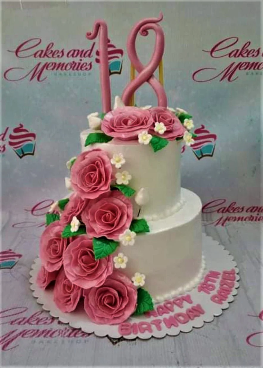 18th Birthday White Floral 2-Tier Debut Cake A white 2-tier 18th Birthday cake, featuring a large pink number 18 topper and pink gumpaste roses.