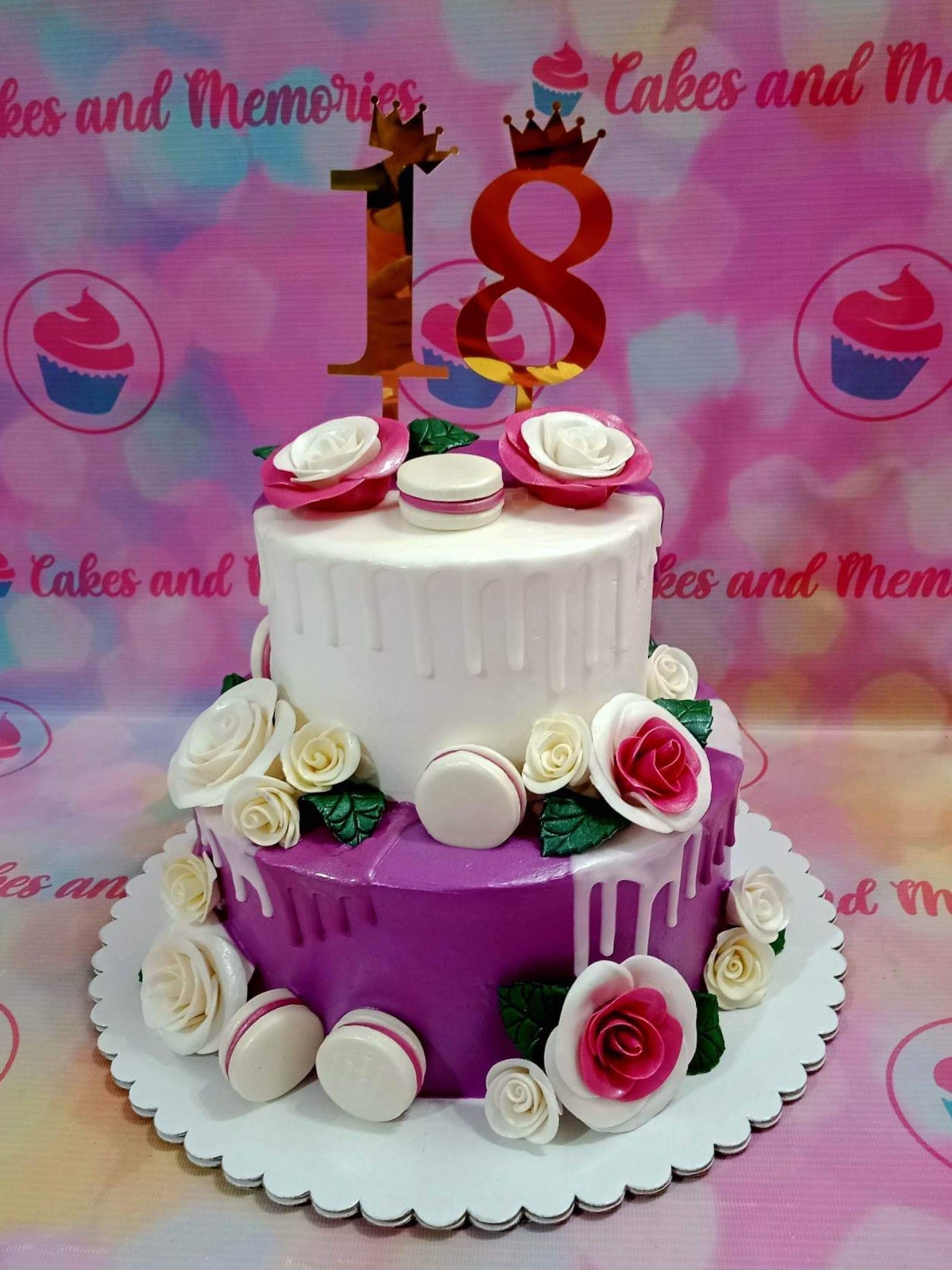 Two-tier purple and white cake with white icing drips, pink and white gumpaste roses, macarons, and a gold number 18 topper. Two-tier purple and white cake with white icing drips, pink and white gumpaste roses, macarons, and a gold number 18 topper.
