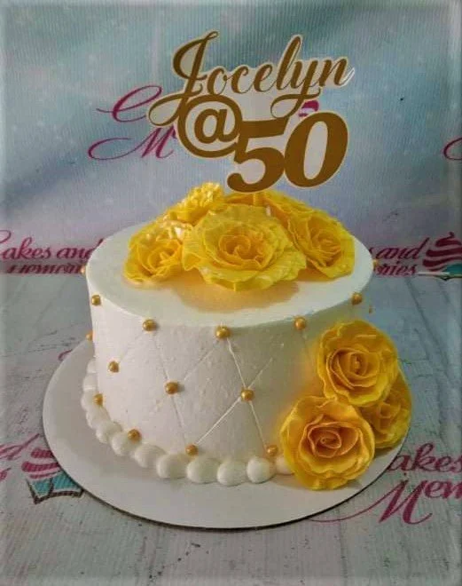 50th Birthday White Floral Cake A white 1-tier 50th birthday cake, featuring a gold Jocelyn @ 50 topper, yellow roses, and a quilted pattern.