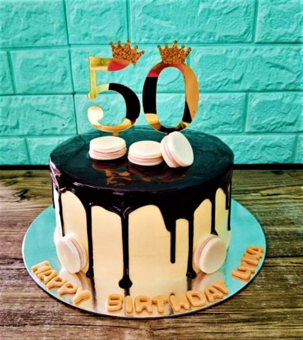 White 1-tier birthday cake with dark chocolate drip, gold 50 topper with crowns, and white macarons. White 1-tier birthday cake with dark chocolate drip, gold 50 topper with crowns, and white macarons.