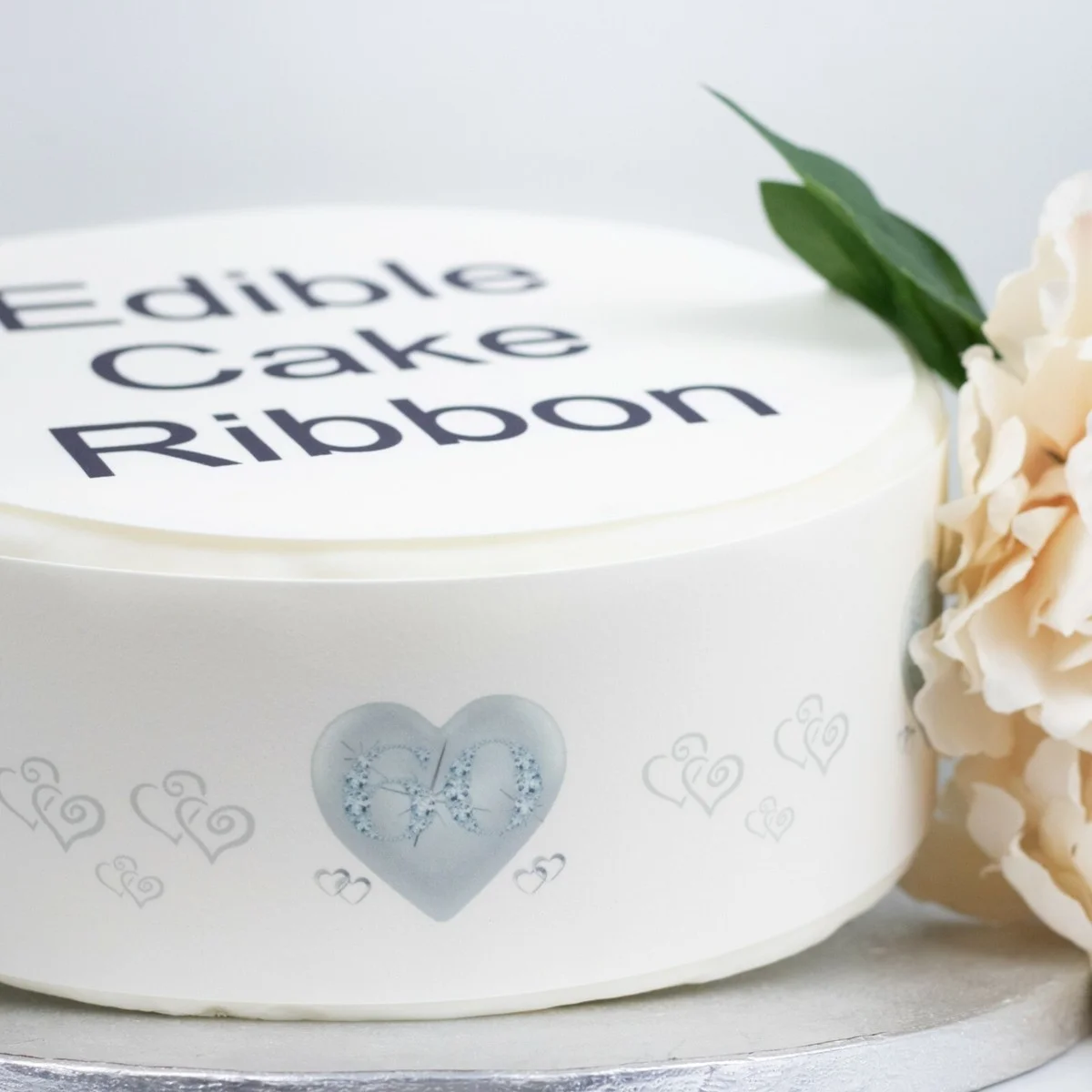 White round cake featuring an edible cake ribbon with a blue heart design and the number 60, topped with large black text. White round cake featuring an edible cake ribbon with a blue heart design and the number 60, topped with large black text.
