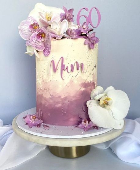 Tall white and purple watercolor cake with fresh orchids, a purple 'Mum' message, and a '60' topper. Tall white and purple watercolor cake with fresh orchids, a purple 'Mum' message, and a '60' topper.