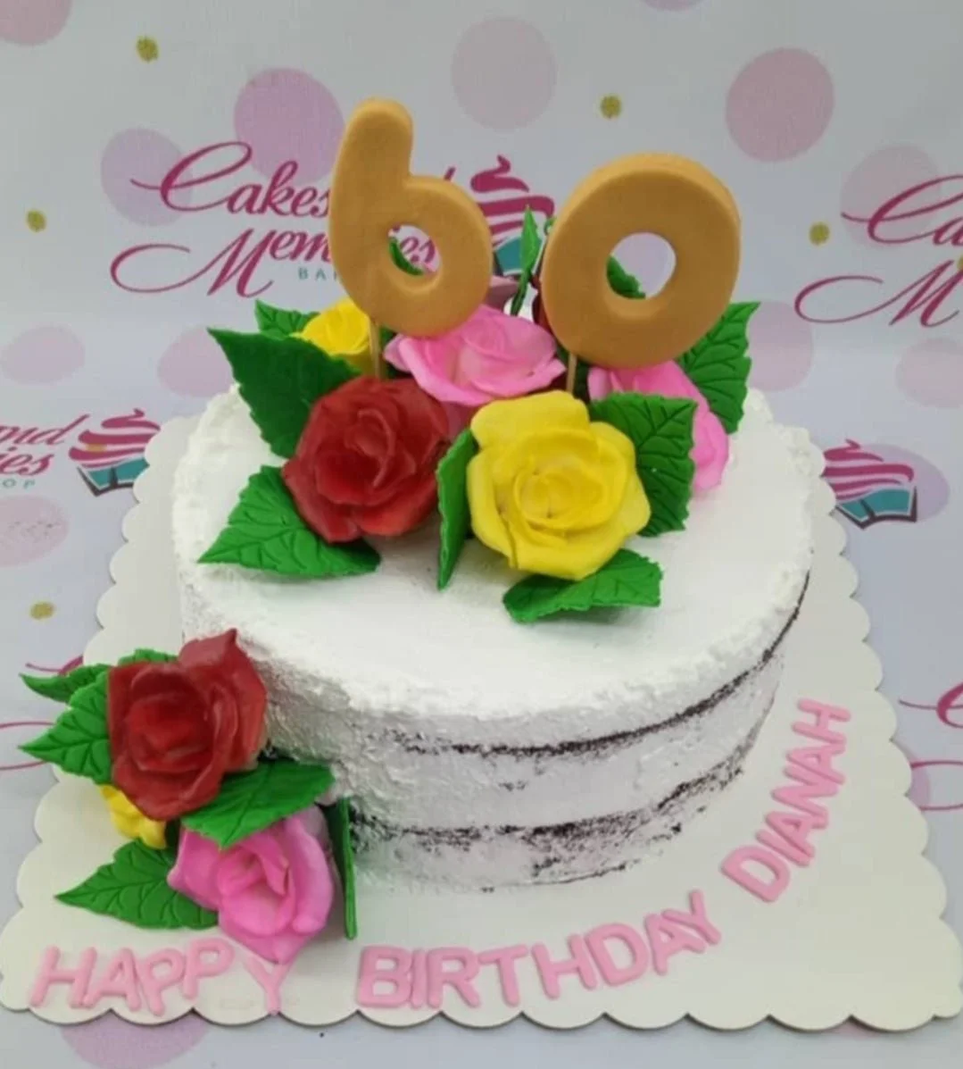 A semi-naked chocolate cake with white icing, red, pink, and yellow gumpaste roses, green leaves, and a gold '60' topper. A semi-naked chocolate cake with white icing, red, pink, and yellow gumpaste roses, green leaves, and a gold '60' topper.