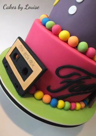 Two-tier 80s themed fondant cake in purple and hot pink with a cassette tape topper and colorful fondant balls. Two-tier 80s themed fondant cake in purple and hot pink with a cassette tape topper and colorful fondant balls.